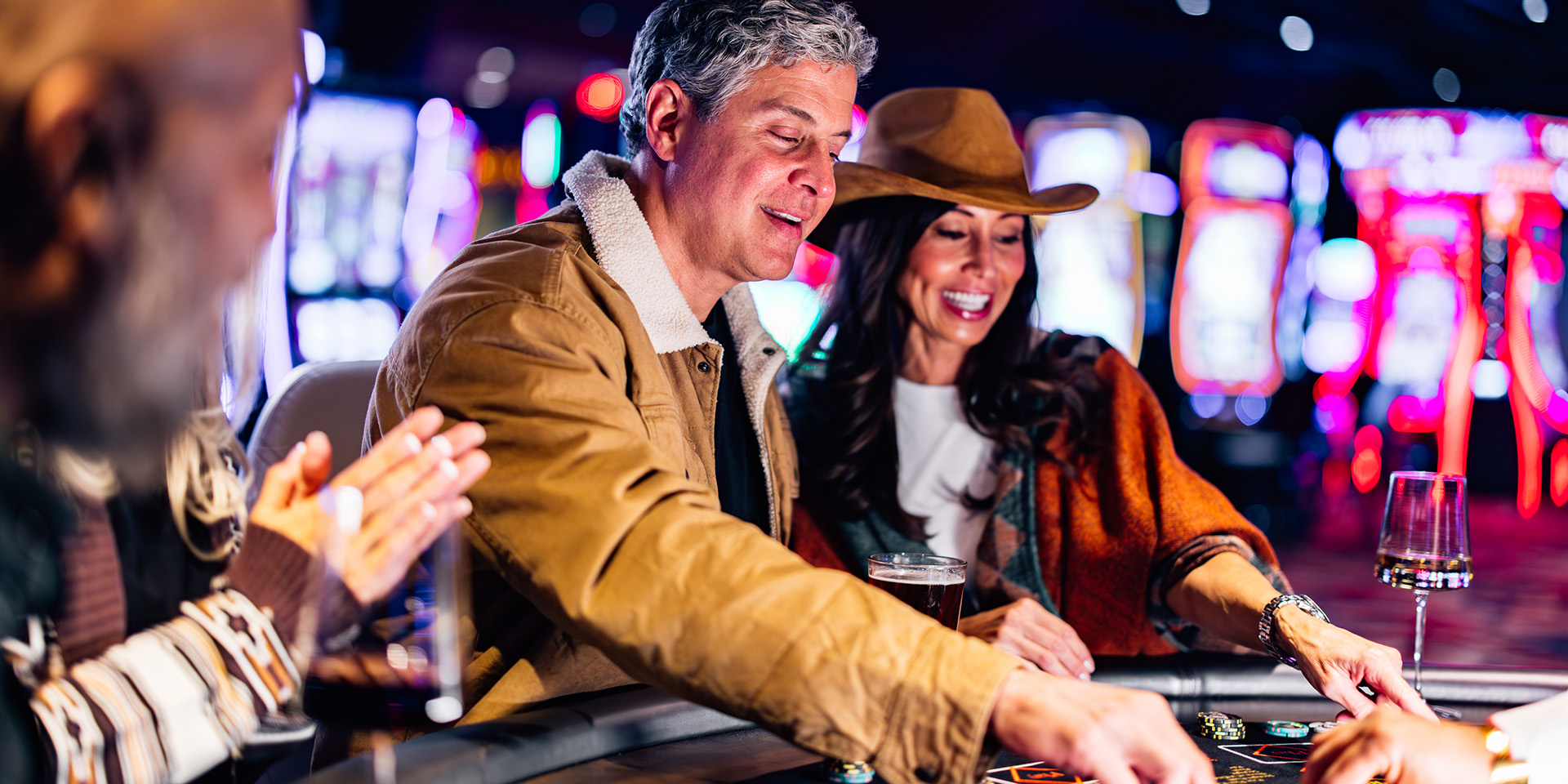 man in leather coat and a woman in a brown cowboy had enjoy a beverage at a poker table